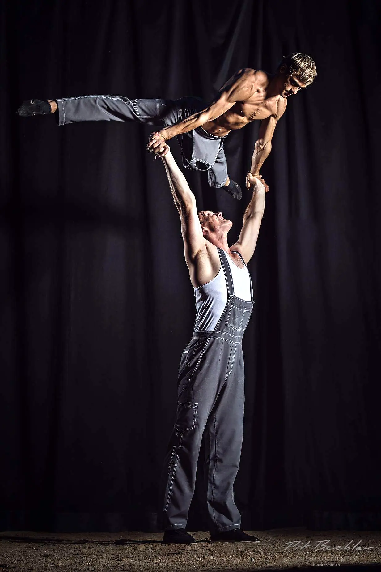 Vertical hand-to-hand balance against a dark curtain