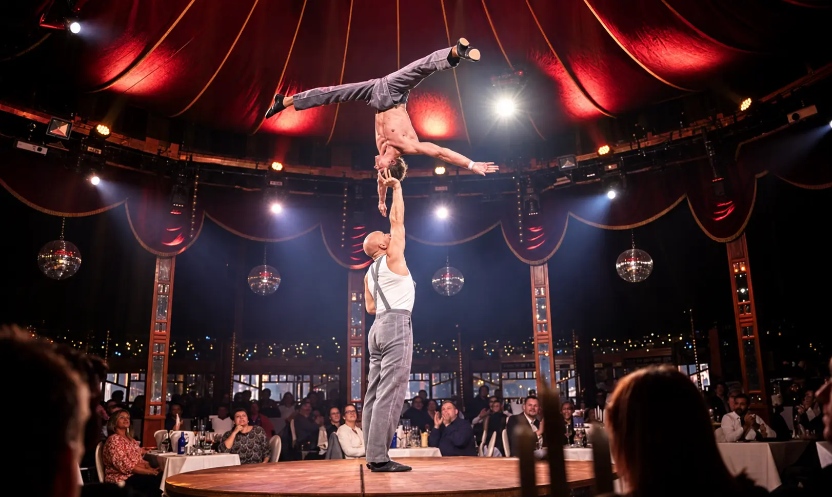 High one-arm balance at night under red circus lighting
