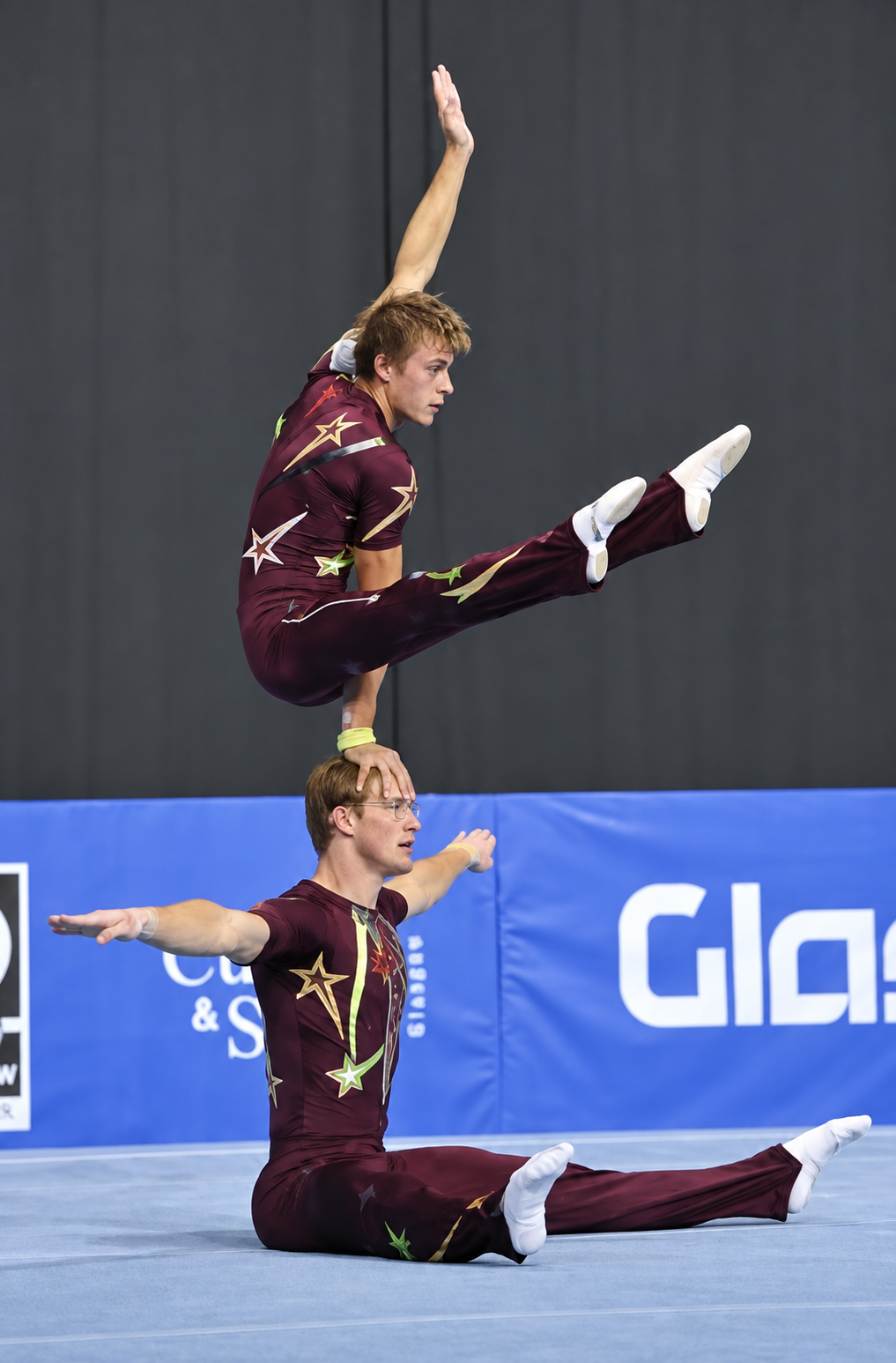 Seated split partner balance in maroon competition costumes